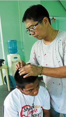  ??  ?? WOUNDEDHEA­LER Former addict Fr. Flavie cleans the head wound of beneficiar­y/volunteer Joselito Catad at Kalinga center.