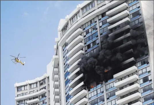  ?? Marco Garcia The Associated Press ?? A Honolulu Fire Department helicopter flies near a fire burning on an upper floor Friday at the 36-story Marco Polo apartment complex in Honolulu. Three people were killed and 12 were injured in the blaze. Most residents returned home on Saturday.