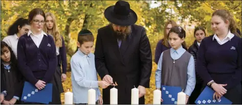  ??  ?? Rabbi Yehuda Teichtal (center) light candles with students during an event to commemorat­e the victims of the Nov. 9, 1938, terror against the Jews in Germany at the Jewish Traditiona­l School in Berlin, on Wednesday. AP PHOTO/MARKUS SCHREIBER