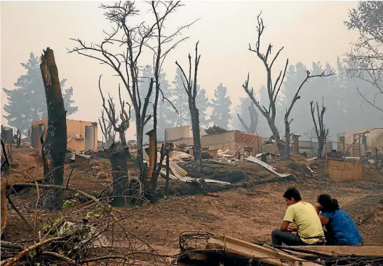  ?? REUTERS ?? A couple sit next to the remains of houses after a wildfire tore through the town of Santa Olga in central Chile, killing 10 people and destroying more than 1000 buildings.