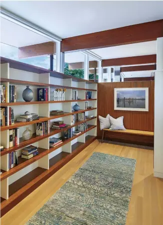  ??  ?? (BOTTOM) SERVING AS AN IDEAL SPOT TO TUCK AWAY AND READ FOR AN AFTERNOON, THE HALLWAY NOW DOUBLES AS A LIBRARY. THE OPEN SHELVING, PROVIDED BY WARREN’S WOOD WORKS INC., IS AMERICAN WALNUT, MIRRORING THE PANELS AND HORIZONTAL LINES IN THE REST OF THE HOME.