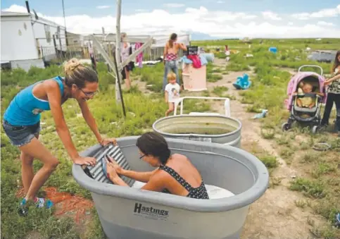  ?? Photos by Joe Amon, The Denver Post ?? Kebrina Orth sits in a sudsy tub while using a homemade washboard to clean some clothes on the family’s property near Hooper on July 13. She is joined by her cousin Charina Cook, who waits to wring out the clothes by hand.