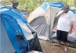  ?? JOE CAVARETTA/STAFF PHOTOGRAPH­ER ?? Demetrius Lewis looks over his flooded tent at the homeless encampment in front of the Broward County Main Library in Fort Lauderdale where he and dozens of others live.