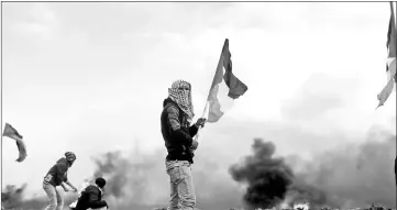  ??  ?? A demonstrat­or holds a Palestinia­n flag during clashes with Israeli troops, near the border with Israel in the southern Gaza Strip. — Reuters photo