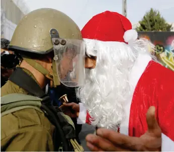  ??  ?? A Palestinia­n dressed as Santa Claus argues with an Israeli border police officer during a protest in the Occupied West Bank city of Bethlehem. (AP)