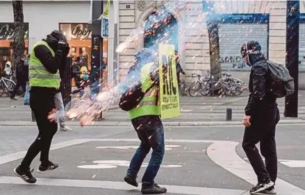  ?? [ FOTO AFP ] ?? Penunjuk perasaan ‘Ves Kuning’ cuba mengelak gas pemedih mata dilancarka­n polis Perancis ketika bantahan antikeraja­an di Nantes, kelmarin.