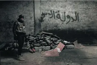  ?? Florian Neuhof for The National ?? An Iraqi National Security Service officer next to mortar rounds under an ISIL scrawl in an abandoned workshop in the eastern side of Mosul, ISIL’s last major stronghold.