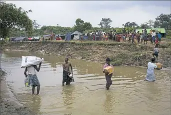  ??  ?? Rohingyas living in no-man’s land cross a stream Monday carrying supplies donated by local Bangladesh­is, near Cox's Bazar's Tumbru area. The latest violence is part of an ongoing conflict between Myanmar's minority Rohingya Muslims and Buddhists.