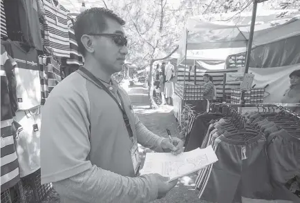  ?? Photo by Jean Nicole Cortes ?? CHECKUP. Harold Halip of the Baguio City Treasurer’s Office inspects the booths at the Market Encounter of the Baguio Blooms for possible violations.