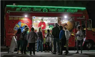  ?? PHOTOS BY ALLEN EYESTONE / THE PALM BEACH POST ?? Redd Johnson serves customers at the Dough Dough Donuts truck at the monthly Food Truck Invasion event in Wellington in October. The owner of four food trucks, Johnson says October is his busiest single month, but he works an average of about 25 events...