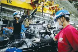  ?? (Issei Kato/Reuters) ?? EMPLOYEES WEARING protective face masks and face guards work on the automobile assembly line at the Kawasaki factory of Mitsubishi Fuso Truck and Bus Corp. south of Tokyo, last month.