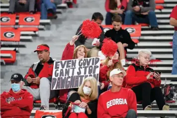  ?? AP Photo/Brynn Anderson, File ?? ■ A fan holds a sign “Even COVID can't stop Dawgmation” before an NCAA college football game Saturday in Athens, Ga. Coaches wearing masks around their chins. Fans not wearing masks at all while cheering from their seats. One school deciding to drop the safety checks it was requiring for those entering the stadium to cut down on long lines. College football is sending plenty of alarming signals at it attempts to get through a tenuous season amid a pandemic.