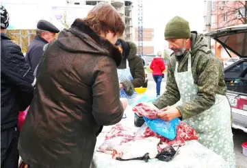  ??  ?? A vendor shows customers a cut of meat at his stall outside a polling station in Donetsk, in the rebel-held area of eastern Ukraine. — AFP photo