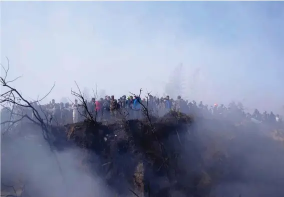  ?? ?? Locals watch the wreckage of a passenger plane in Pokhara, Nepal, yesterday. Photo: AP/Yunish Gurung.