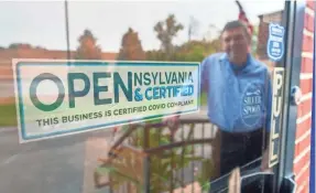  ?? PAUL KUEHNEL/USA TODAY NETWORK ?? David LeHeron, the owner of the Blue Heron, is reflected in the window displaying his Certified COVID Compliant sign at the main entrance of the Springetts­bury Township, Pa., restaurant.