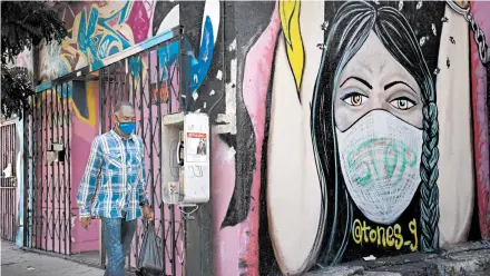  ?? JAE C. HONG/AP ?? A man wearing a face mask walks past a mural Wednesday in Los Angeles. The U.S. is averaging 40,000 virus cases a day.