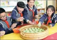  ?? DING TING / XINHUA ?? Elementary school students from Shanghai put qingtuan, green snacks for Tomb Sweeping Day made of sticky rice and mugwort, into a steamer on Saturday.