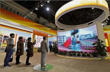  ??  ?? Visitors watching a man appearing on a screen as he experience­s a national anthem flag raising ceremony at an exhibition highlighti­ng China’s achievemen­ts at the Beijing Exhibition Hall in the capital city where the 19th Party Congress is held in...