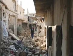  ?? (Alaa Faqir/Reuters) ?? A MAN walks between damaged buildings yesterday in the rebel-held Tariq al-Sad neighborho­od of Deraa, Syria.