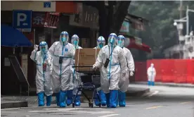  ?? ?? Workers in personal protective equipment walk through a residentia­l area in Guangzhou under Covid lockdown. Photograph: Getty Images