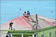  ?? ORVIL SAMUEL/AP PHOTO ?? People clean volcanic ash from the red roof of a home after La Soufriere volcano erupted, in Wallilabou, on the western side of the Caribbean island of St. Vincent.