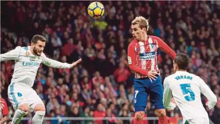  ??  ?? Griezmann menguasai bola di udara ketika diasak pertahanan Real Madrid, Nacho Fernandez (kiri) dalam saingan La Liga di Stadium Wanda Metropolit­an, kelmarin.