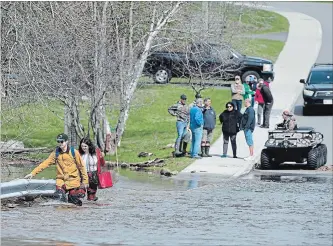  ?? ANDREW VAUGHAN THE CANADIAN PRESS ?? Simon Barton, left, and Chelsea Burley wear makeshift waders of garbage bags and packing tape as they cross a flooded road in Saint John, N.B. on Sunday.