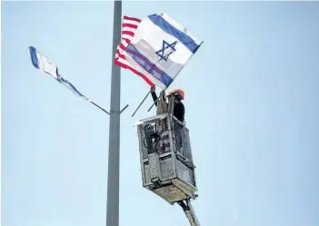  ?? ARIEL SCHALIT/THE ASSOCIATED PRESS ?? A worker hangs Israeli and American flags on a lamppost along a freeway leading to Jerusalem, days before a planned visit by U.S. President Donald Trump, Tuesday.