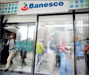  ?? AP/FERNANDO LLANO ?? A customer leaves a Banesco bank branch Friday as others wait in line in Caracas, Venezuela.