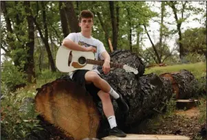  ?? The Associated Press ?? PARADISE, CALIF.: Del Smith plays his guitar in fire-burned trees near where his family’s home was destroyed by the 2018 Camp Fire in Paradise, Calif., on April 15. Del, a graduating senior and football player at Paradise High School, often returns to the site of his childhood home and says playing his guitar is an outlet for the emotions tied to his memories of the fire and current crises in the world. He says hardship has taught him to take challenges in stride. “This coming generation’s going to have a hard life. Something’s going to happen,” he says. “But we’re ready for it, I guess.”