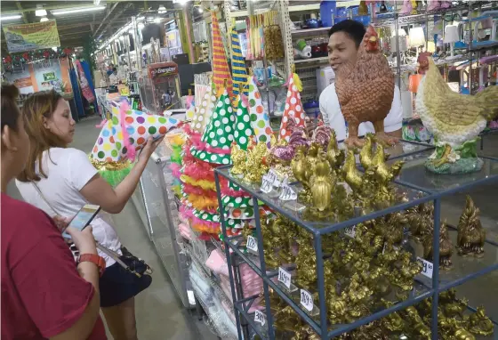  ?? (SUN.STAR FOTO/ALAN TANGCAWAN) ?? WILL IT BE SOMETHING TO CROW ABOUT? New Year’s Eve shoppers examine a display of party hats (with polka dots, of course) and, for those who believe in Chinese geomancy, figurines for the Year of the Fire Rooster, which will begin later this month.