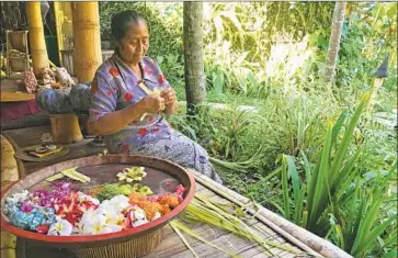  ??  ?? AT BAMBU INDAH hotel, a Balinese woman makes offerings of f lowers and woven bamboo to the spirits.