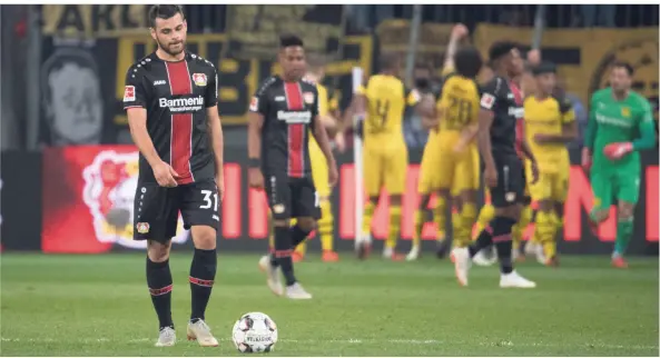  ?? FOTO: DPA ?? Leverkusen­s Angreifer Kevin Volland schreitet Richtung Anstoß, während Dortmund das zwischenze­itliche 2:3 bejubelt.