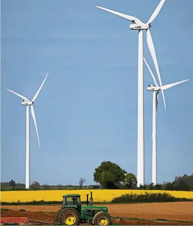  ??  ?? Environmen­t friendly: A tractor of a French farmer is pictured in his field in front of power-generating windmill turbines on a wind park in Pamproux, France. Green bonds are used to raise funds for projects which help tackle environmen­tal problems...