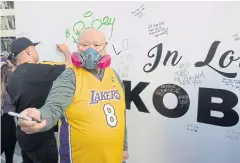  ??  ?? SAFETY FIRST: A Lakers fan wears a mask to protect against the coronaviru­s at a Staples Centre memorial wall to NBA legend Kobe Bryant on Friday.