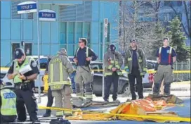  ?? REUTERS ?? Fire fighters stand near a covered body at a major intersecti­on in Toronto on Monday.