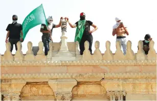  ?? (Ammar Awad/Reuters) ?? A MAN HOLDS a Hamas flag as he stands next to others atop a building near al-Aqsa Mosque in Jerusalem’s Old City on Monday.