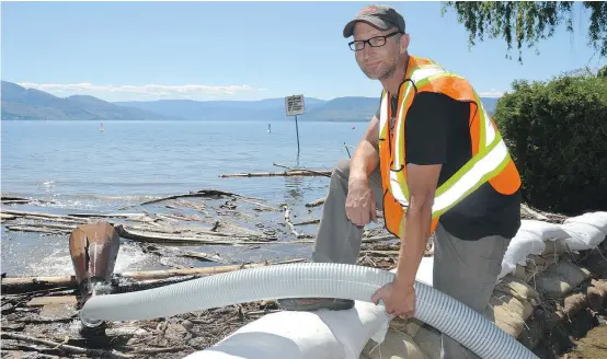  ?? — RON SEYMOUR/KELOWNA DAILY COURIER ?? Derek Enns installed a larger pipe from storm drains under a sandbagged section of Bluebird Road into Okanagan Lake on Monday. Hot temperatur­es are expected to increase the flow of Mission Creek into the lake.