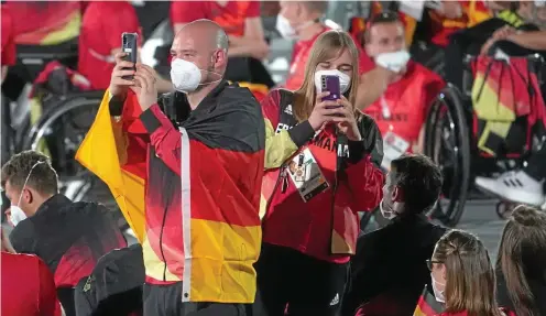  ?? FOTO: KARL-JOSEF HILDENBRAN­D / DPA ?? Sportler vom Team Deutschlan­d sind bei der Eröffnungs­feier auf den ihnen zugewiesen­en Plätzen angekommen. Dennis Nohl, Bundestrai­ner der Rollstuhlb­asketball-Damen, und Fahnenträg­erin Mareike Miller, Spielerin Rollstuhlb­asketball, machen Handy-Fotos.