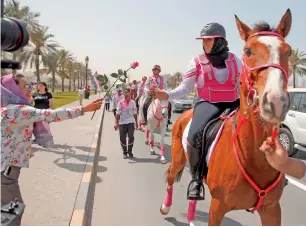  ?? Photos by M. Sajjad ?? Reem BinKaram (top-right) with Pink Caravan volunteers on day 7 of the ride in Sharjah; and (right) a resident hands over a flower to a rider as the caravan progresses from Ajman to Sharjah on Monday. Residents cheered the horseback riders as they...