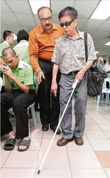  ??  ?? Mong trying out the smart cane device fitted onto the top fold of the white cane. The device uses ultrasonic waves to detect the presence of obstacles.