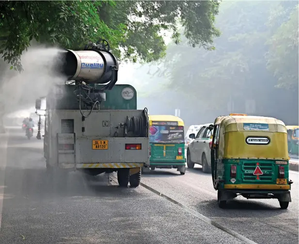  ?? ?? Commuters ride past an anti-smog gun spraying water to curb air pollution amid heavy smog conditions in New Delhi. — AFP