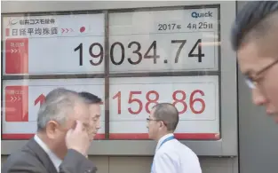  ?? Reuters — ?? Pedestrian­s walk by an electronic board showing Japan’s Nikkei average outside a brokerage in Tokyo.