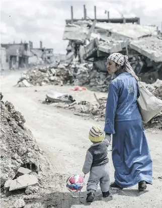  ??  YASIN AKGUL/AFP/GETTY IMAGES ?? A Kurdish woman walks with her child past the ruins of the town of Kobane, Syria, on Wednesday. Federal politician­s will begin debate Thursday on striking ISIL targets in the country.