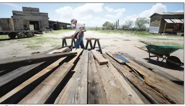  ??  ?? Tom Kimmel cuts lumber salvaged from the damaged buildings and structures while helping repair the boardwalk outside the main saloon on the Mescal Movie Set.