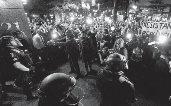  ?? JEFF SINER, TRIBUNE NEWS SERVICE ?? Protesters confront police officers in riot gear in Charlotte, North Carolina, on Thursday. Unlike Tuesday and Wednesday, Thursday’s protest remained peaceful after night fell. Members of the U.S. National Guard were deployed, and a midnight curfew was...