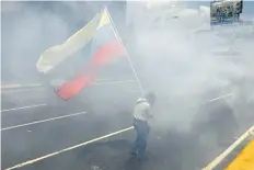  ?? ARIANA CUBILLOS/AP PHOTO ?? A man walks with a Venezuelan flag amid tear gas launched by security forces blocking opponents to President Nicolas Maduro from marching to the Ombudsman’s office in downtown Caracas, Venezuela, Wednesday.