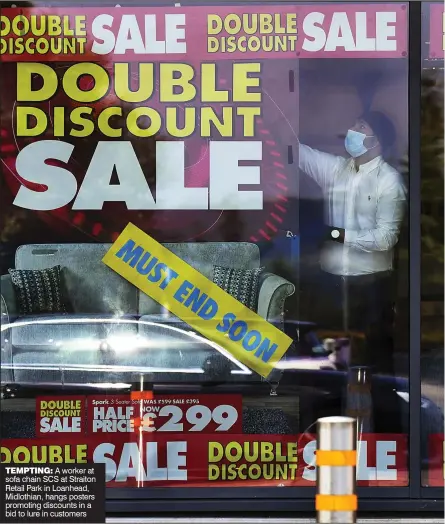  ??  ?? TEMPTING: A worker at sofa chain SCS at Straiton Retail Park in Loanhead, Midlothian, hangs posters promoting discounts in a bid to lure in customers