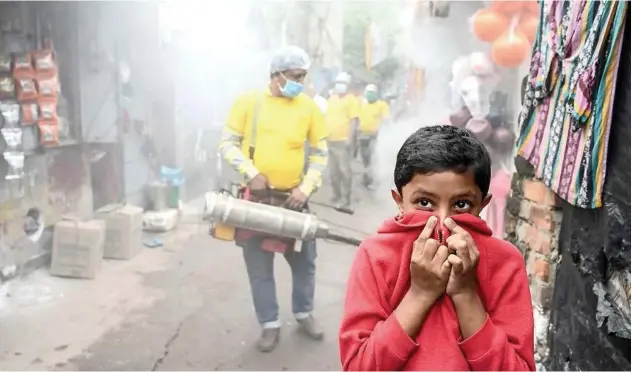  ?? Agence France-presse ?? ↑
A child covers his face while a municipal worker fumigates a slum area as a preventive measure against mosquitobo­rn diseases in Kolkata on Monday.