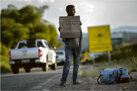  ?? Mauro Pimentel - 27.fev.2018/AFP ?? Refugiado venezuelan­o carrega cartaz pedindo trabalho e carona na estrada que liga a fronteira com a Venezuela com Boa Vista, em Pacaraima (RR)